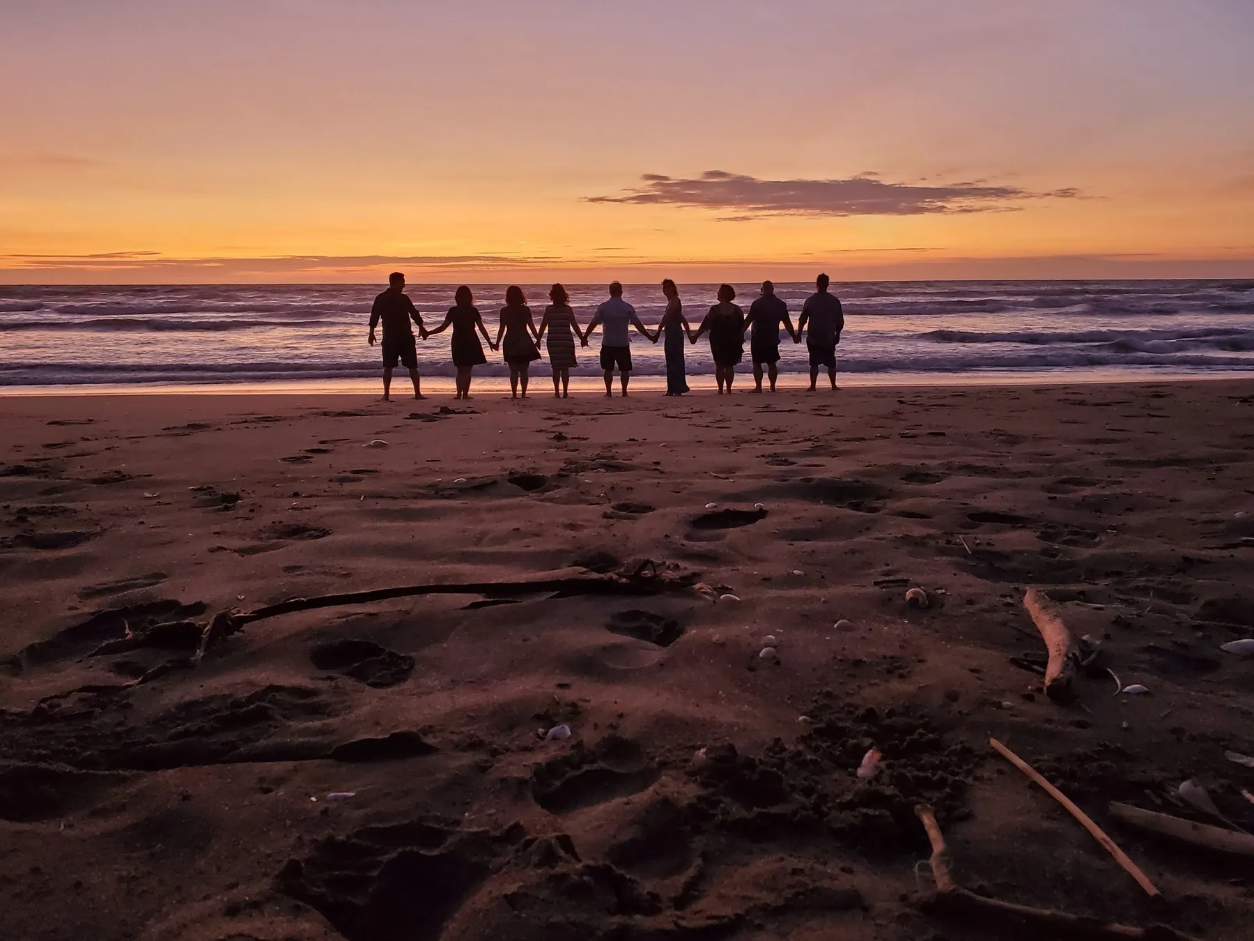 Group holding hands facing the sea at sunset in Canoa